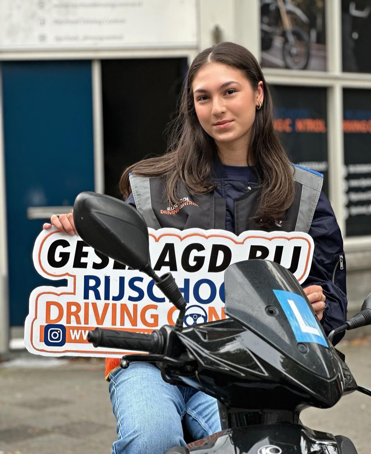 Geslaagde scooterleerling in scooterkleding met Geslaagd-bord Rijschool Driving Control Rotterdam