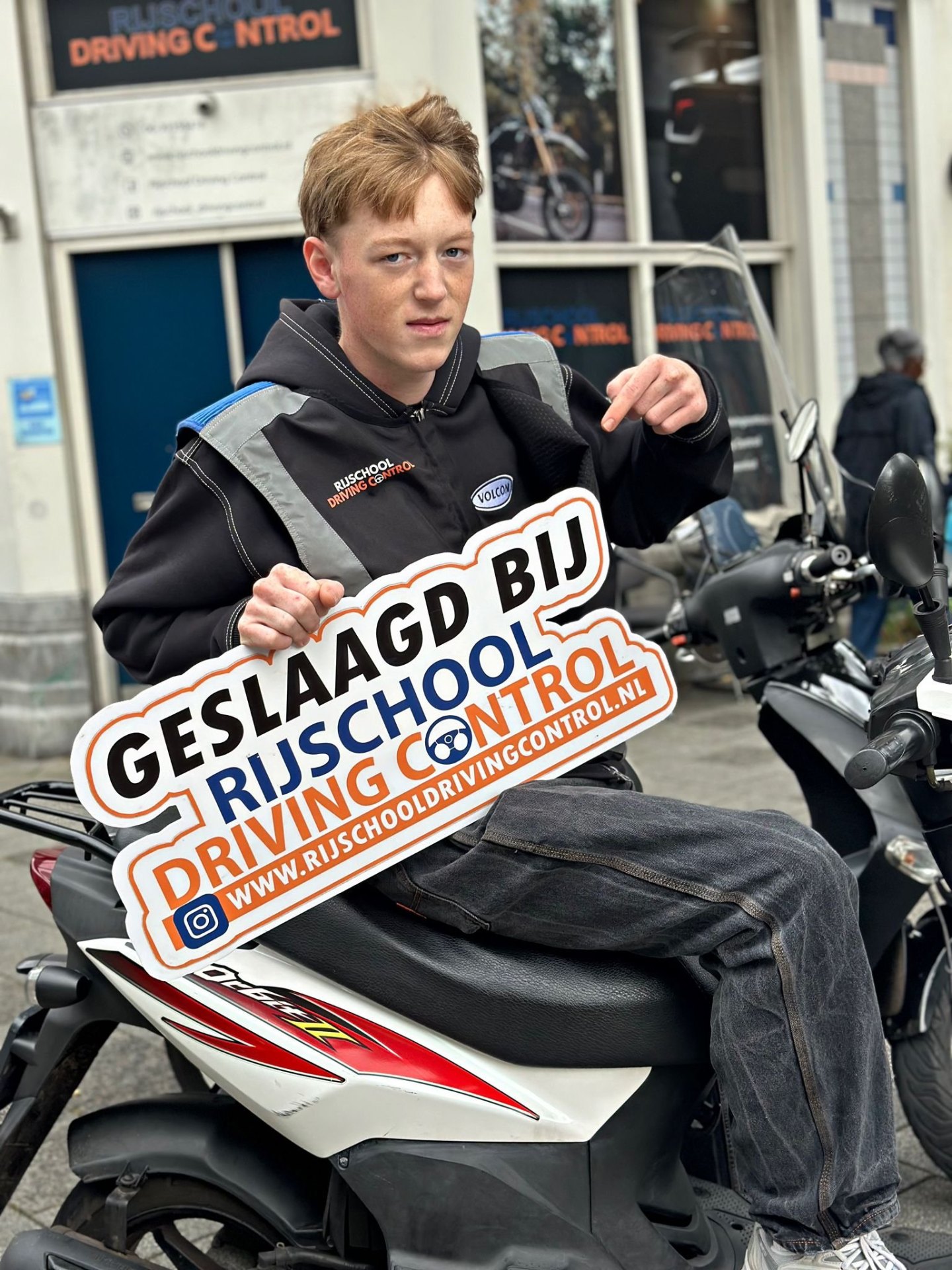 Geslaagde scooterleerling op scooter met Geslaagd-bord Rijschool Driving Control Rotterdam